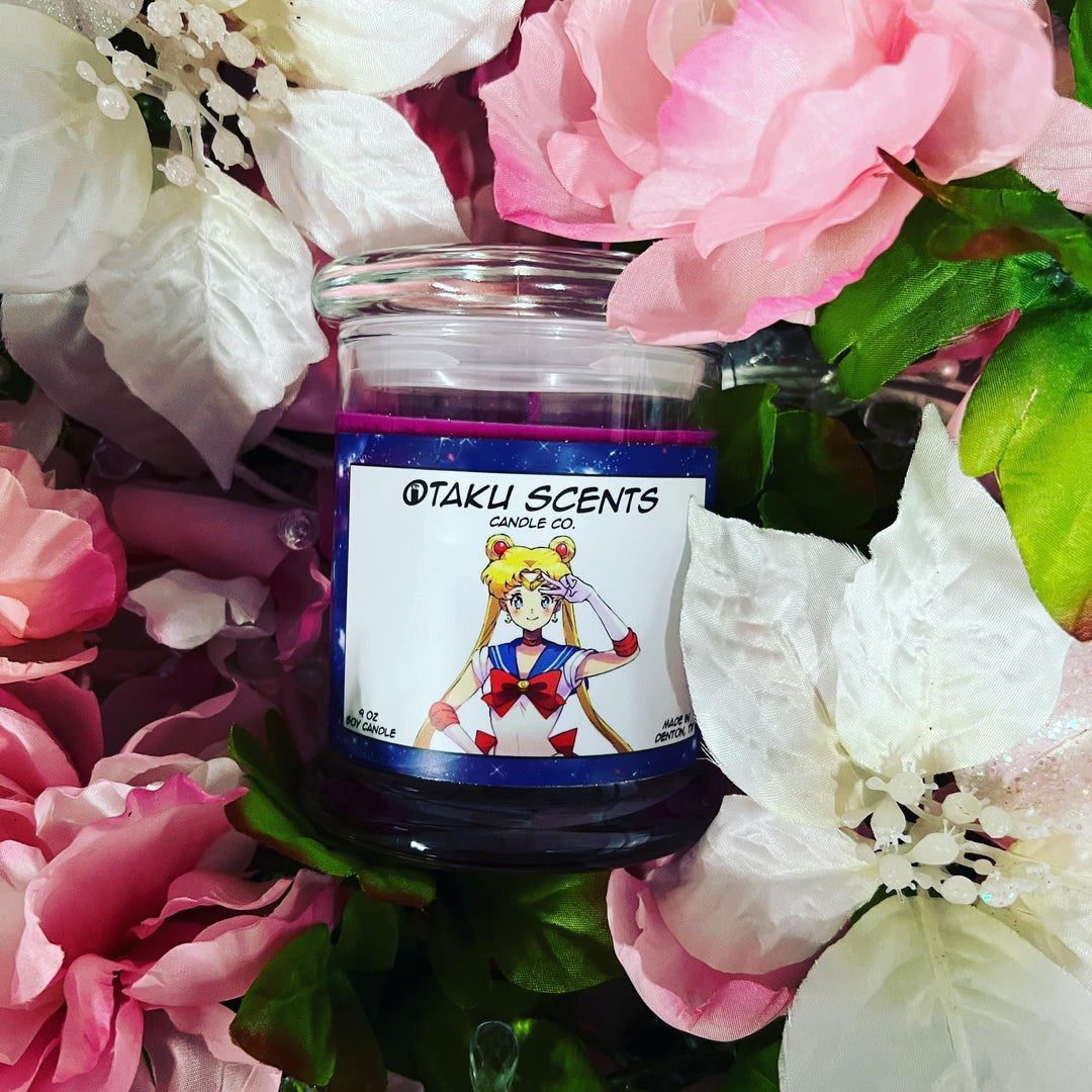 Otaku Scents branded candle with lid, with anime character Sailor Moon on the label. Candle is surrounded by various faux flowers.
